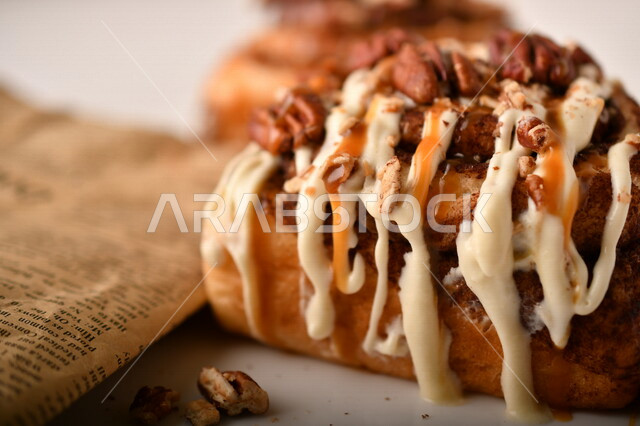 صورة مقربة للفائف القرفة اللذيذة المزينة بالجوز و الصوص الابيض، لفائف السينابون، معجنات، سينابون رول ، مخبوزات طازجة، لفائف الحلوى الشهية 