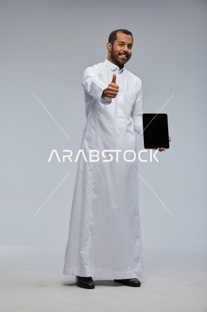 رجل سعودي بالثوب يحمل جهاز لوحي في الاستوديو