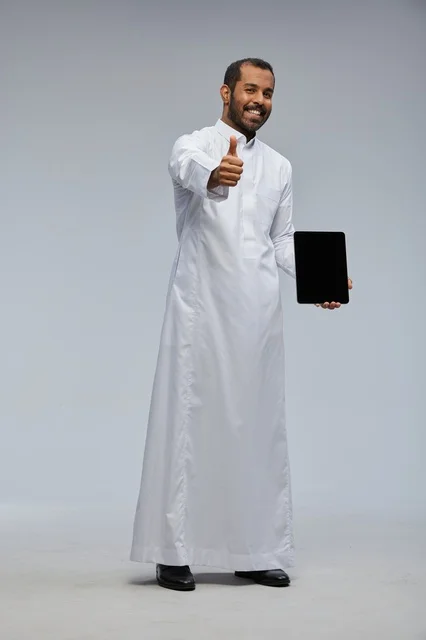 رجل سعودي بالثوب يحمل جهازاً لوحياً مع إشارة الإعجاب