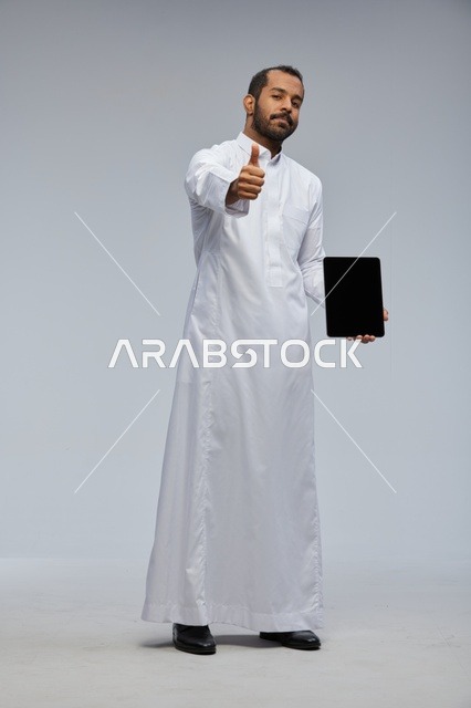رجل سعودي بالثوب الأبيض مع جهاز لوحي وإيماءة نجاح