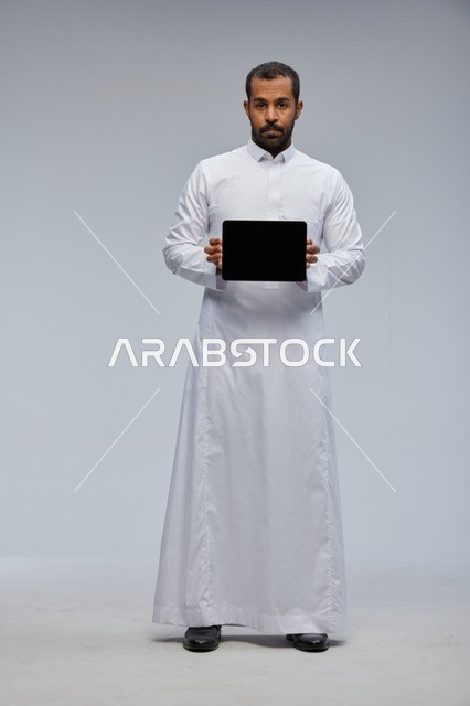 رجل سعودي بالثوب التقليدي يحمل جهاز لوحي أسود