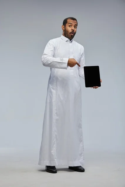 Saudi Man in White Thobe Pointing at Tablet Screen