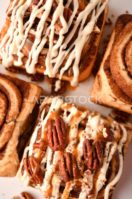 صورة مقربة للفائف القرفة اللذيذة المزينة بالجوز و الصوص الابيض، لفائف السينابون، معجنات، سينابون رول ، مخبوزات طازجة، لفائف الحلوى الشهية 