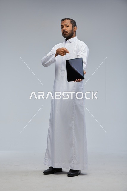 رجل سعودي بالثوب الأبيض يحمل جهاز لوحي