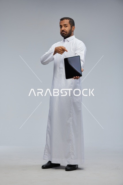 رجل سعودي بالثوب الأبيض يحمل جهاز لوحي ذكي
