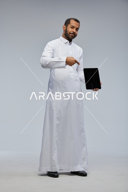 رجل سعودي بالثوب الأبيض يحمل جهاز لوحي