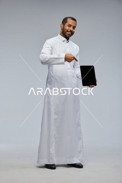 رجل سعودي بالثوب الأبيض يحمل جهازاً لوحياً