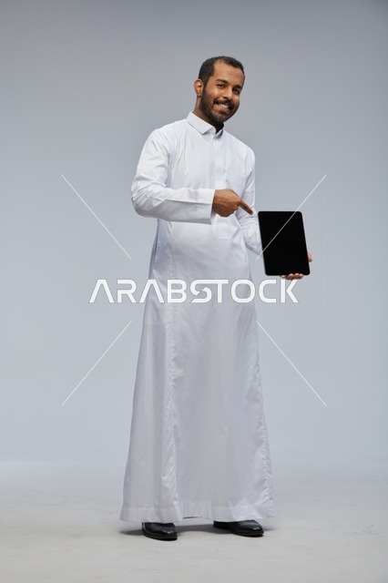 رجل سعودي بالثوب الأبيض يمسك بجهاز لوحي