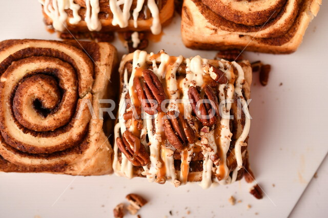 صورة مقربة للفائف القرفة اللذيذة المزينة بالجوز و الصوص الابيض، لفائف السينابون، معجنات، سينابون رول ، مخبوزات طازجة، لفائف الحلوى الشهية 
