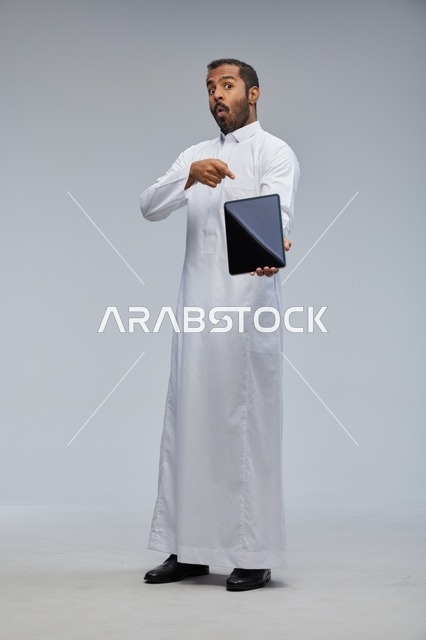 رجل سعودي بالثوب الأبيض يشير لجهاز لوحي في استوديو