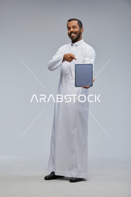 رجل سعودي بالثوب الأبيض يحمل جهازاً لوحياً