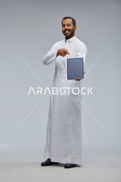رجل سعودي بالثوب الأبيض يشير إلى جهاز لوحي رقمي