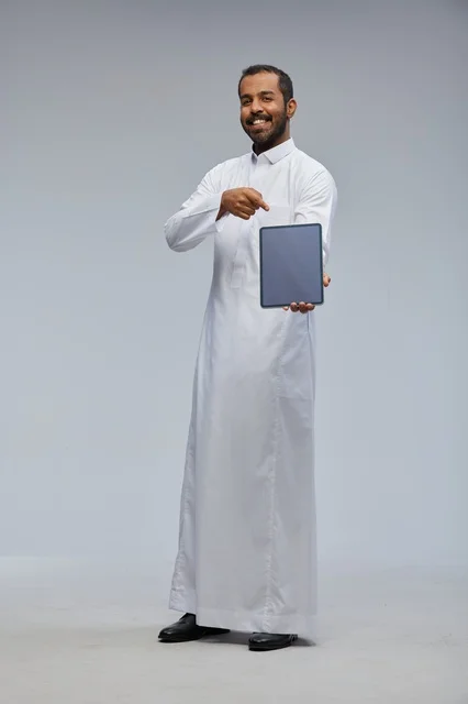 رجل سعودي بالثوب الأبيض يشير إلى جهاز لوحي رقمي