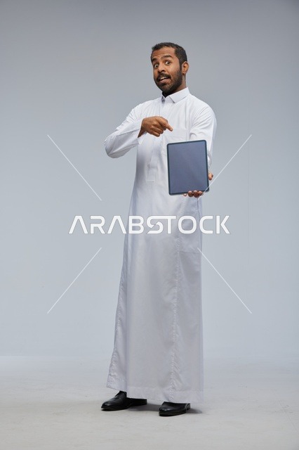 رجل سعودي بالثوب التقليدي يحمل جهاز لوحي