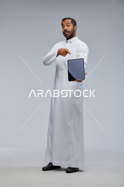 رجل سعودي بالثوب الأبيض يشير إلى جهاز لوحي رقمي