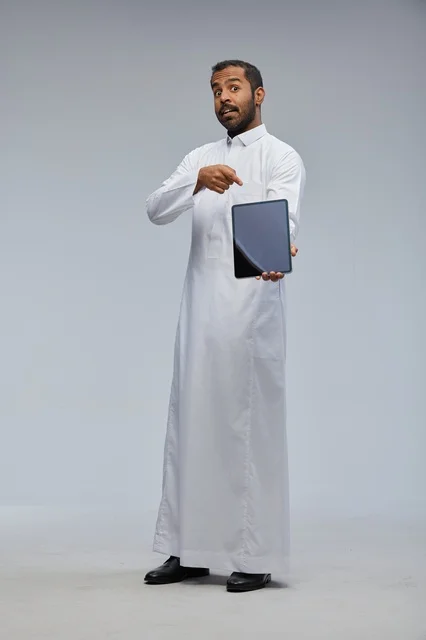 رجل سعودي بالثوب الأبيض يشير إلى جهاز لوحي رقمي