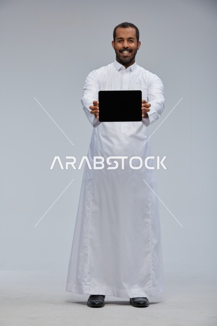 رجل سعودي بالثوب الأبيض يحمل جهازاً لوحياً