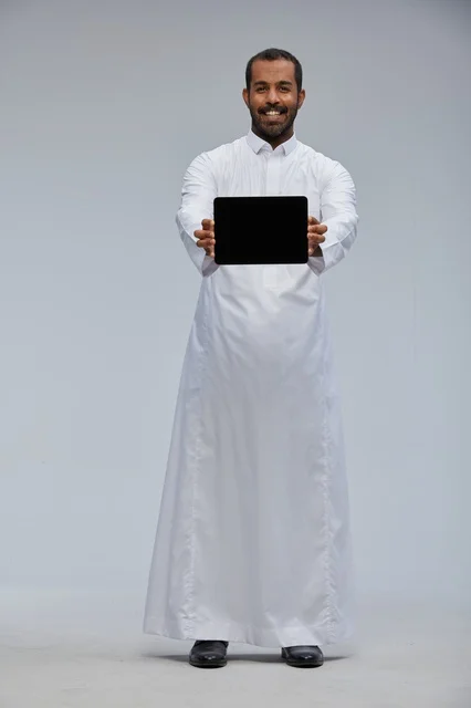 Saudi Man in White Thobe Holding Digital Tablet