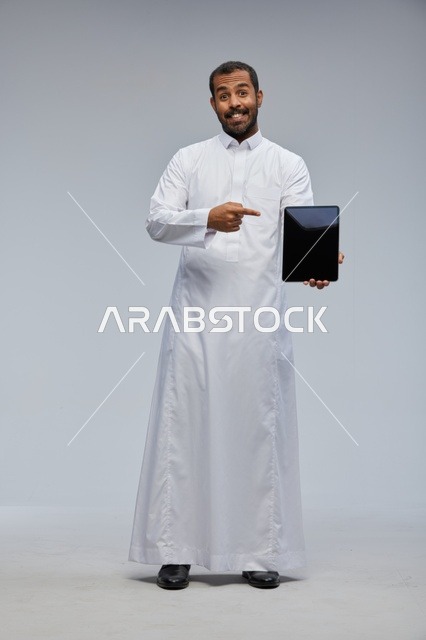 رجل سعودي بالثوب الأبيض يشير إلى جهاز لوحي
