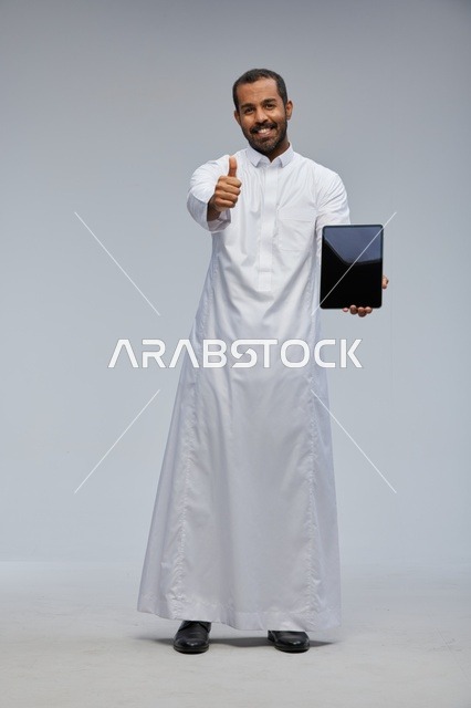 رجل سعودي بالثوب الأبيض يمسك جهاز لوحي بعلامة إعجاب