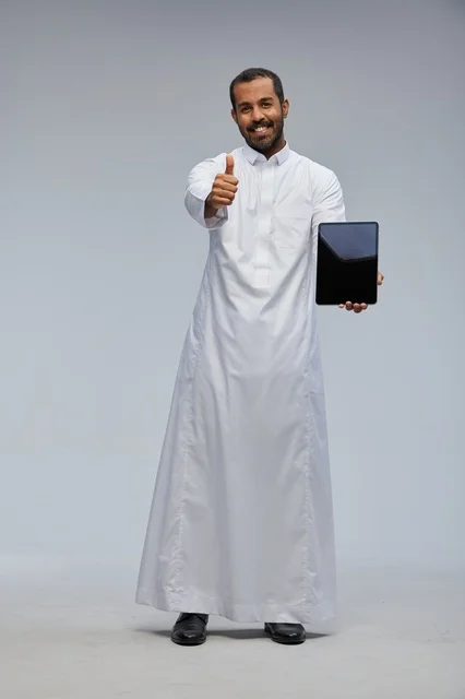 رجل سعودي بالثوب الأبيض يمسك جهاز لوحي بعلامة إعجاب
