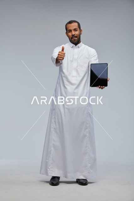 رجل سعودي بالثوب التقليدي يحمل جهاز لوحي