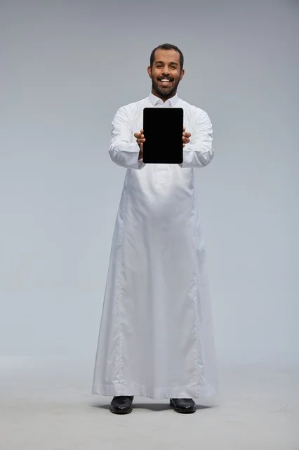 رجل سعودي بالثوب الأبيض التقليدي يمسك جهازاً لوحياً