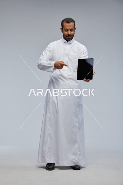 رجل سعودي يرتدي ثوباً أبيض يمسك جهازاً لوحياً