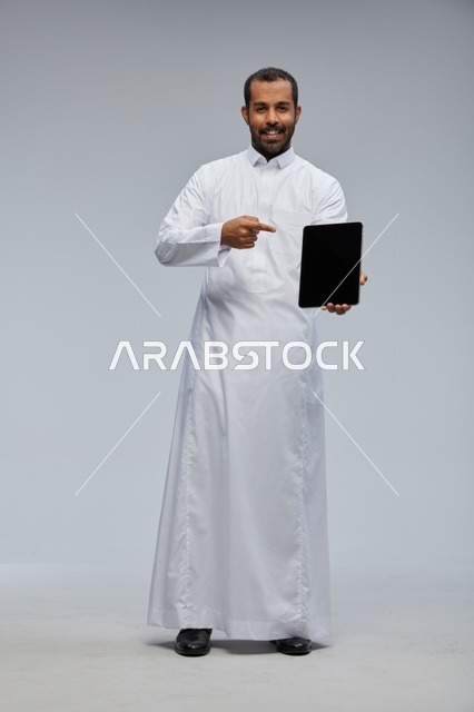 رجل سعودي يرتدي الثوب الأبيض ويعرض جهاز لوحي رقمي