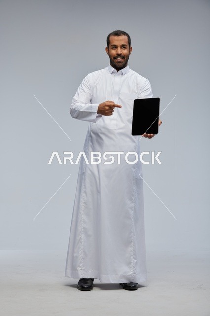 رجل سعودي يرتدي الثوب الأبيض يشير إلى جهاز لوحي ذكي