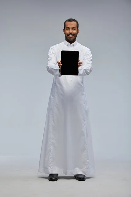 رجل سعودي بالثوب الأبيض يمسك جهازاً لوحياً في الاستوديو