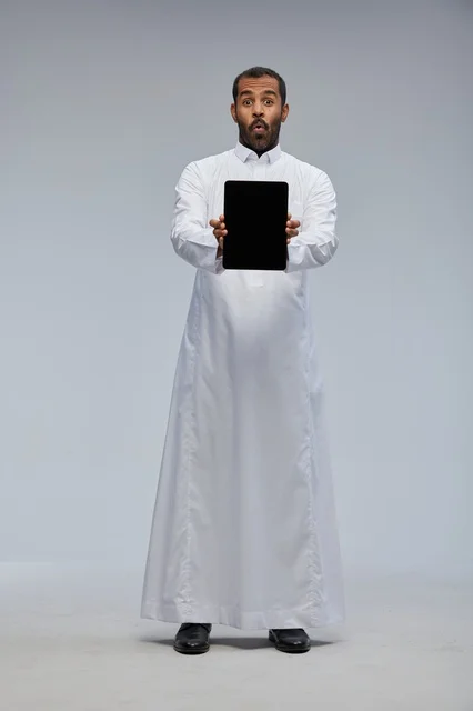 رجل سعودي بالثوب الأبيض يحمل جهازاً لوحياً