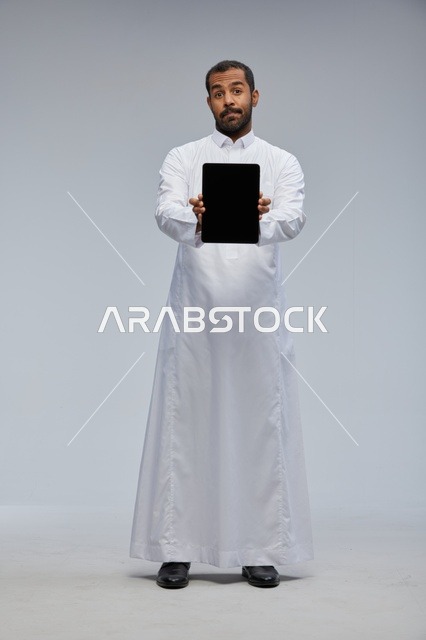 رجل سعودي بالثوب الأبيض يمسك جهازاً لوحياً