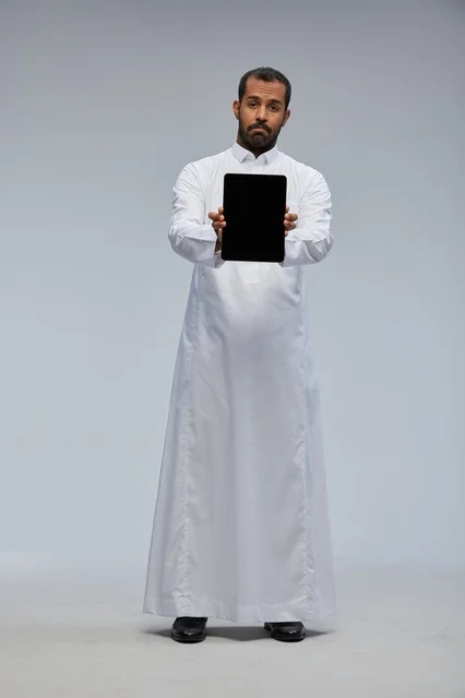رجل سعودي بالثوب الأبيض يحمل جهاز لوحي في الاستوديو