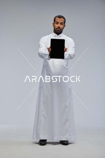 رجل سعودي بالثوب الأبيض يحمل جهاز لوحي