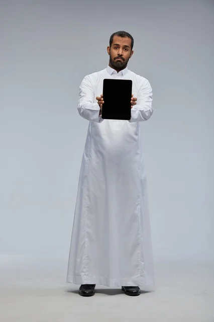 Saudi Man in White Thobe Holding Digital Tablet
