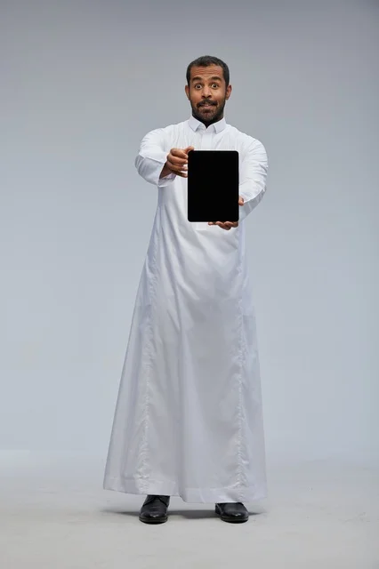 رجل سعودي بالثوب الأبيض يحمل جهاز لوحي في استوديو