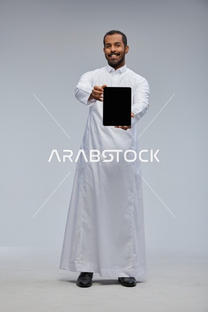 رجل سعودي بالثوب الأبيض يمسك بجهاز لوحي