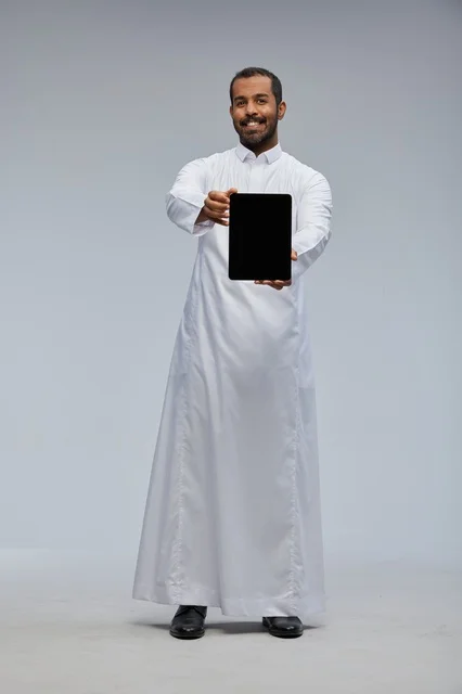 رجل سعودي بالثوب الأبيض يمسك بجهاز لوحي