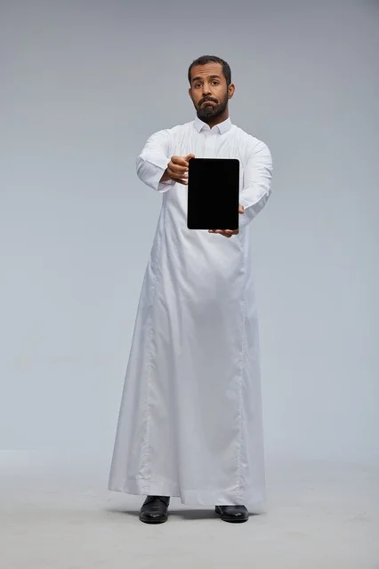 رجل سعودي بالثوب الأبيض يحمل جهاز لوحي في استوديو