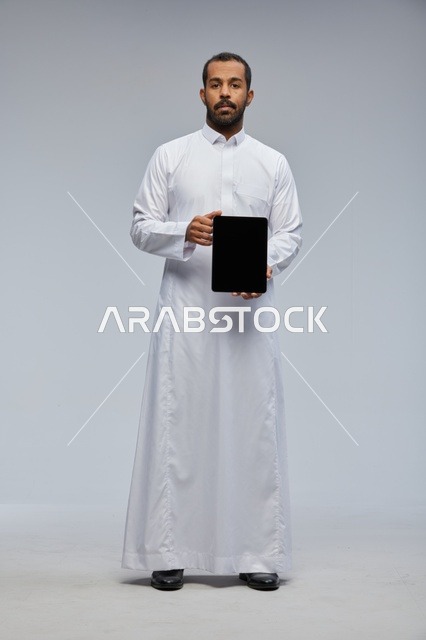 رجل سعودي يرتدي الثوب الأبيض ويمسك جهاز لوحي رقمي