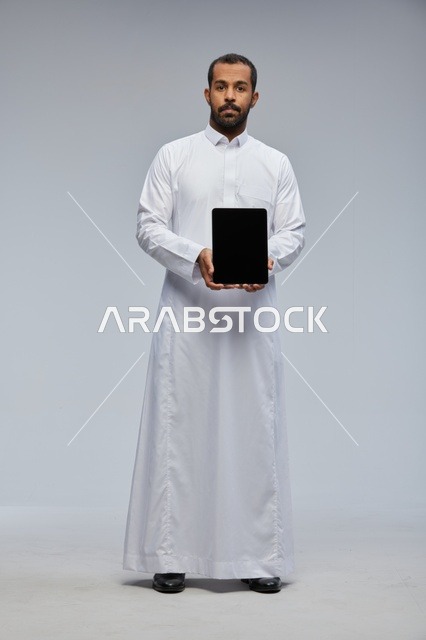 رجل سعودي بالثوب التقليدي يحمل جهاز لوحي