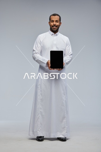 رجل سعودي بالثوب التقليدي يمسك بجهاز لوحي