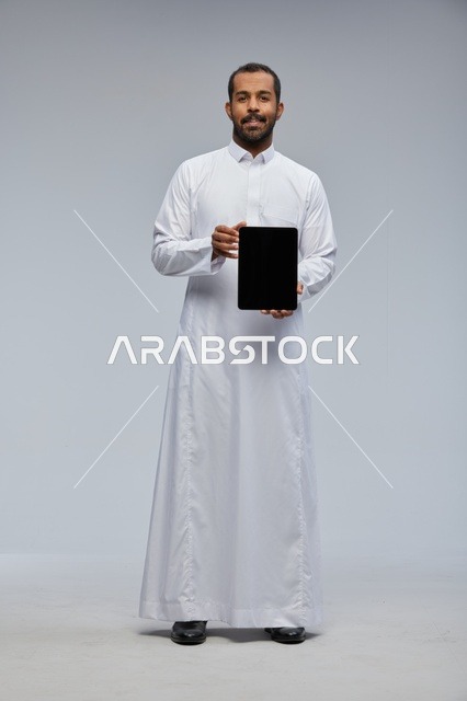 رجل سعودي بالثوب الأبيض يمسك جهاز لوحي رقمي
