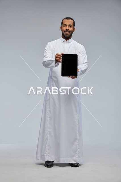 رجل سعودي بالثوب الأبيض يحمل جهاز لوحي في الاستوديو