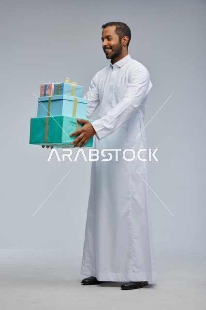 رجل سعودي بالثوب الأبيض يحمل صناديق هدايا مغلفة