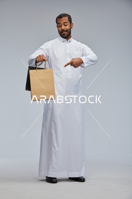 رجل سعودي بالثوب يحمل أكياس تسوق في الاستوديو