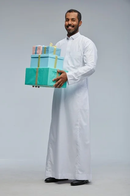 رجل سعودي بالزي التقليدي يحمل صناديق هدايا ملونة
