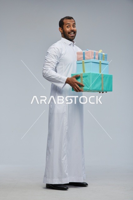 رجل سعودي بالثوب يحمل صناديق هدايا ملونة في الاستوديو