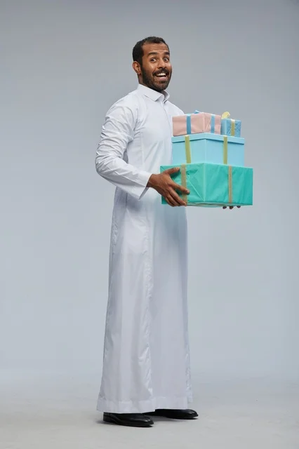 رجل سعودي بالثوب يحمل صناديق هدايا ملونة في الاستوديو